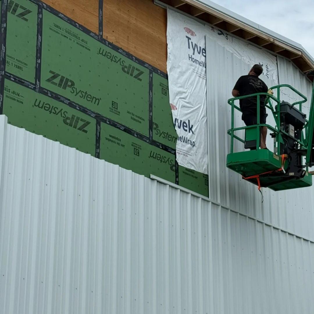 Worker on a lift installing metal siding over house wrap and sheathing